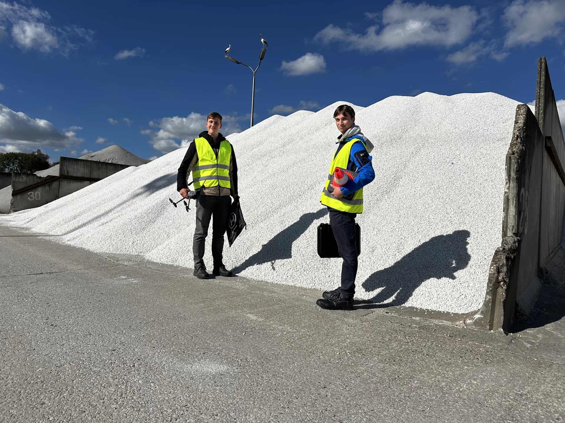 Twee MRR Drones-collega's in hi-vis op locatie bij een grote grondstoffenberg op een depot